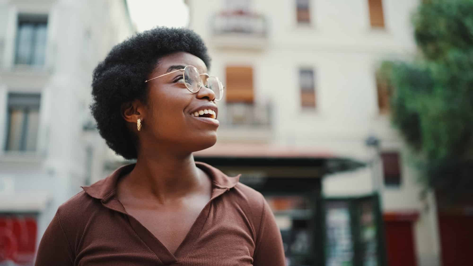 Portrait of Afro American dark haired girl looking cheerful walk around city. Happy expression